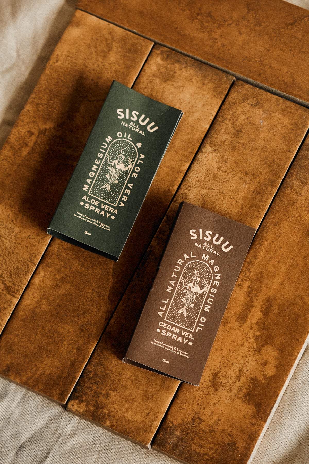 SISUU 5ml magnesium spray samples in green Recovery and brown Cedar Veil boxes on a wooden table